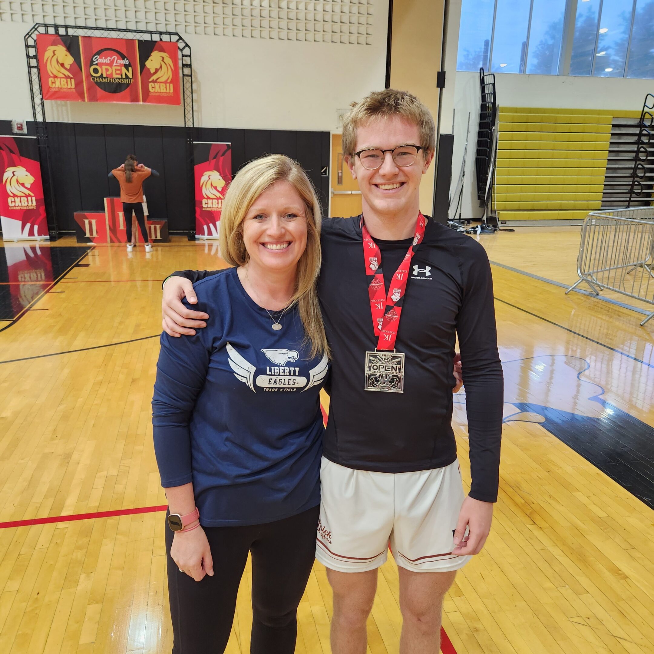 A woman and man posing together in a gymnasium, smiling at the camera.
