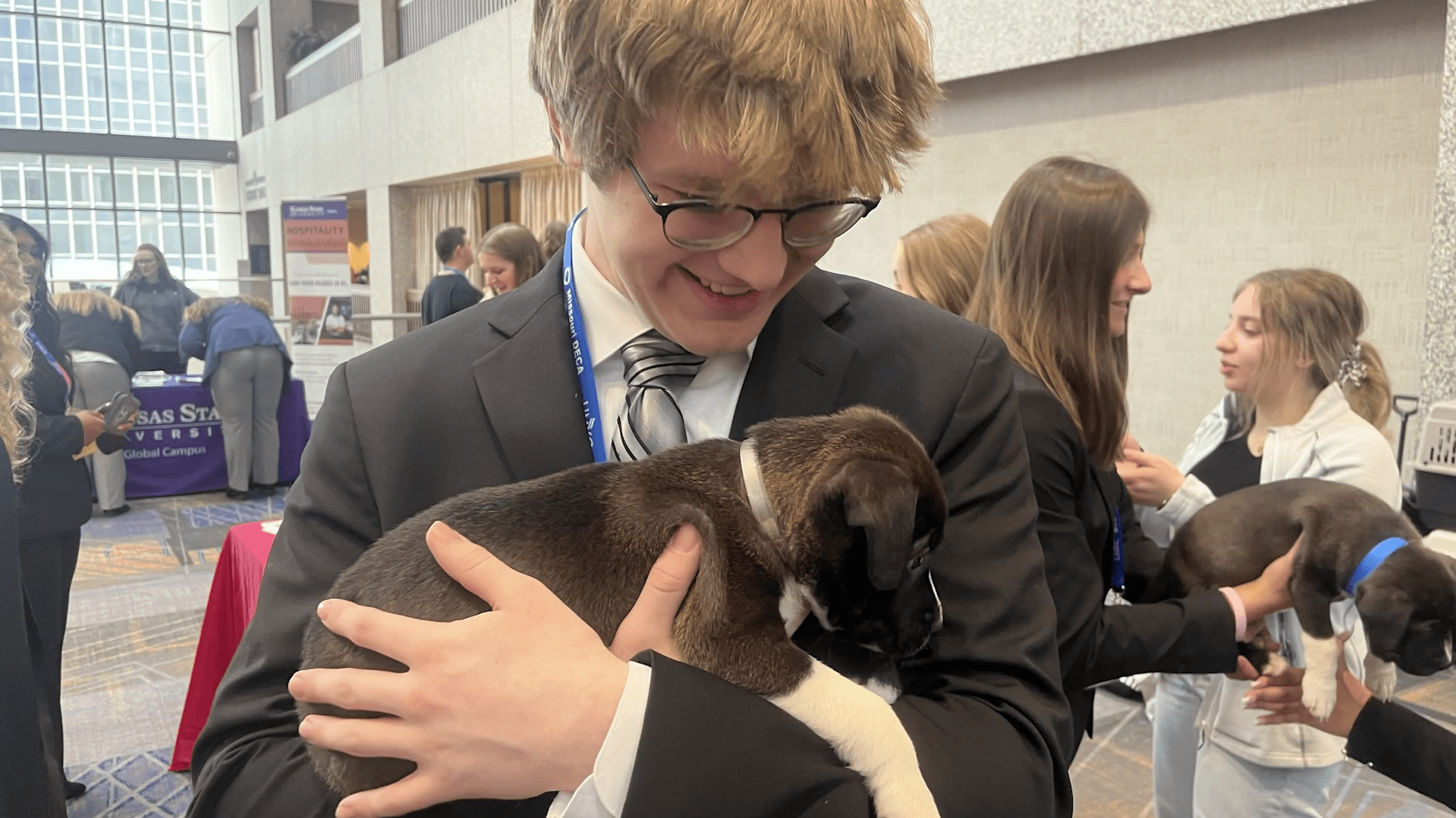 Young person in formal attire holding a small puppy and smiling.