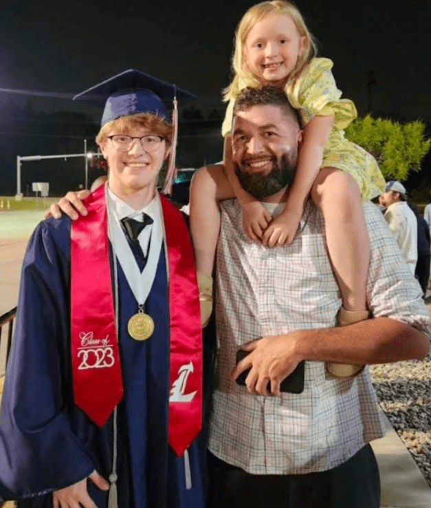 Graduate with cap and gown celebrates with family outdoors at night.